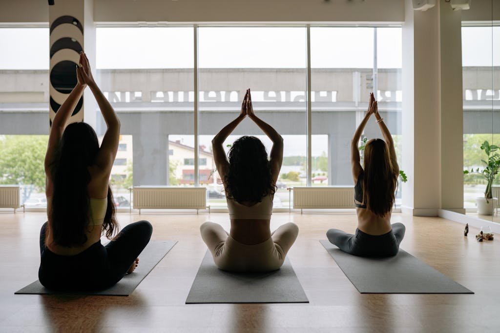 Three women performing yoga poses on mats in a sunlit studio. The scene exudes tranquility and focus.